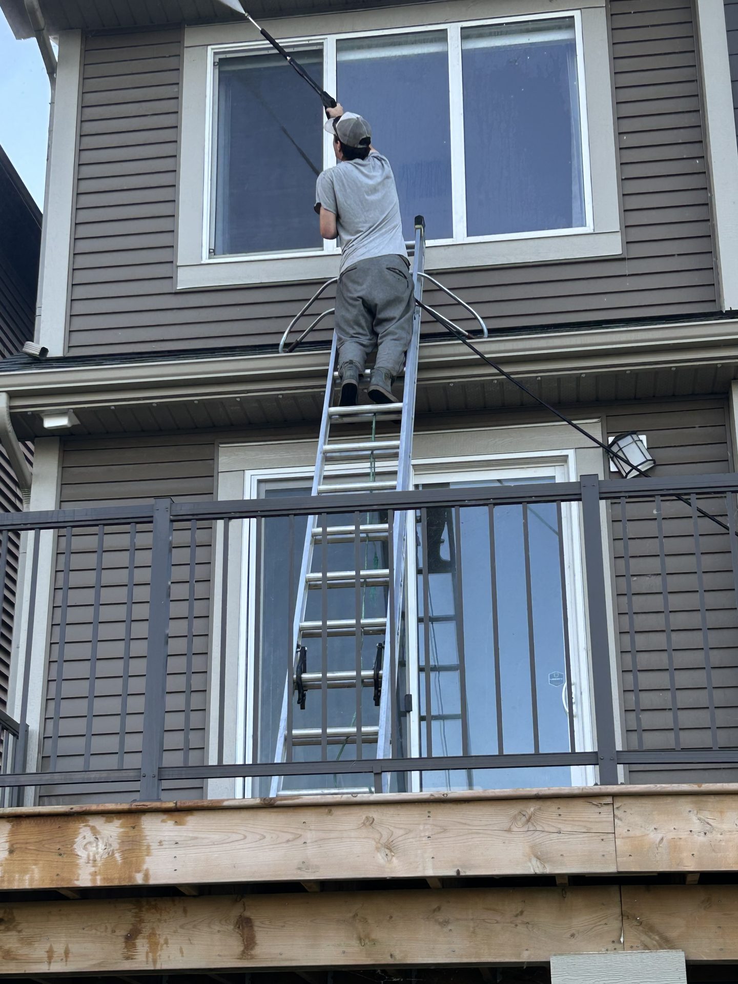 A Squeegee Guys technician cleaning second-storey windows with a pole